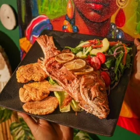 Pescado frito entero servido con patacones y ensalada sobre una tabla de madera